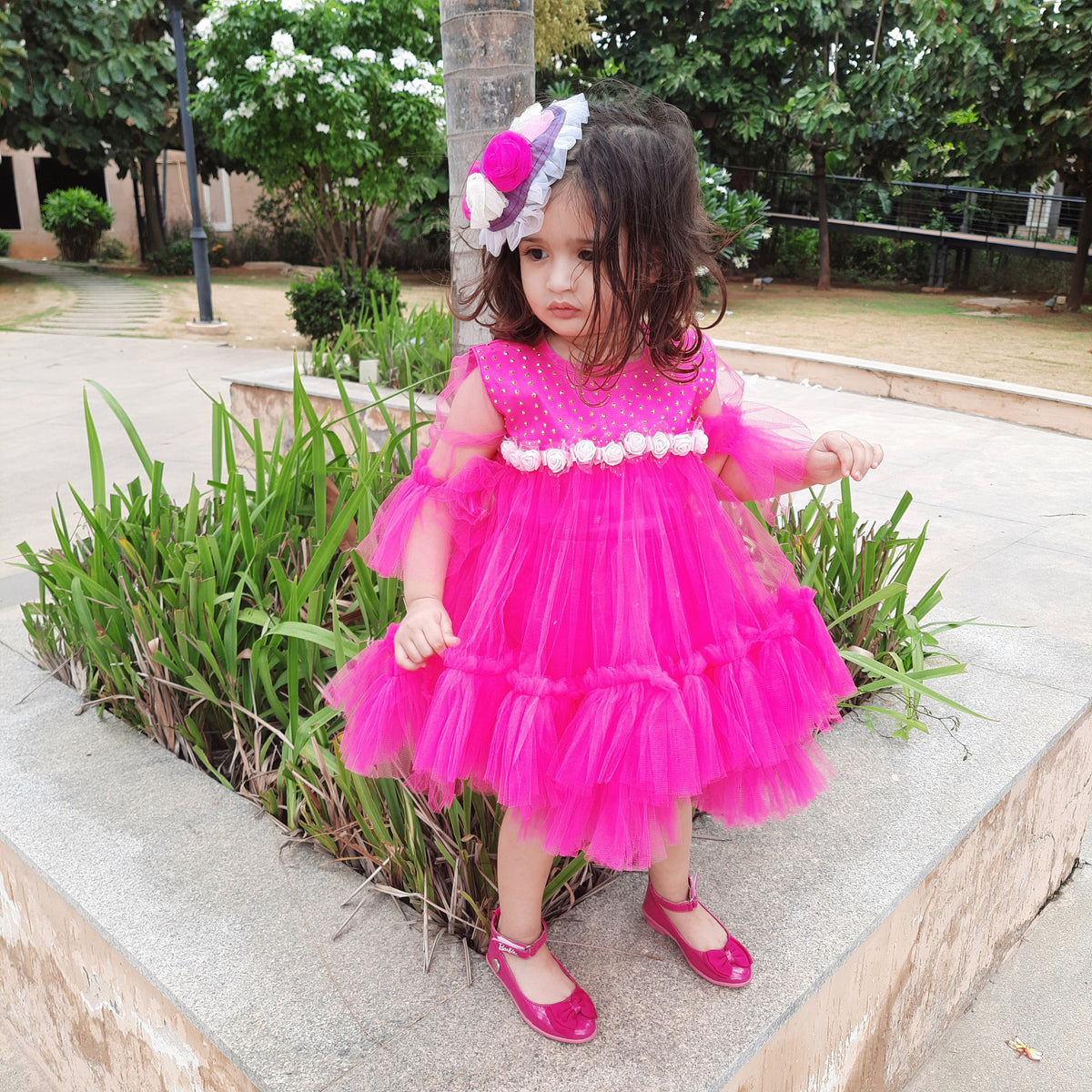 Girl wearing a hot pink layered tulle partywear frock with decorative rose waist detailing by Hovea